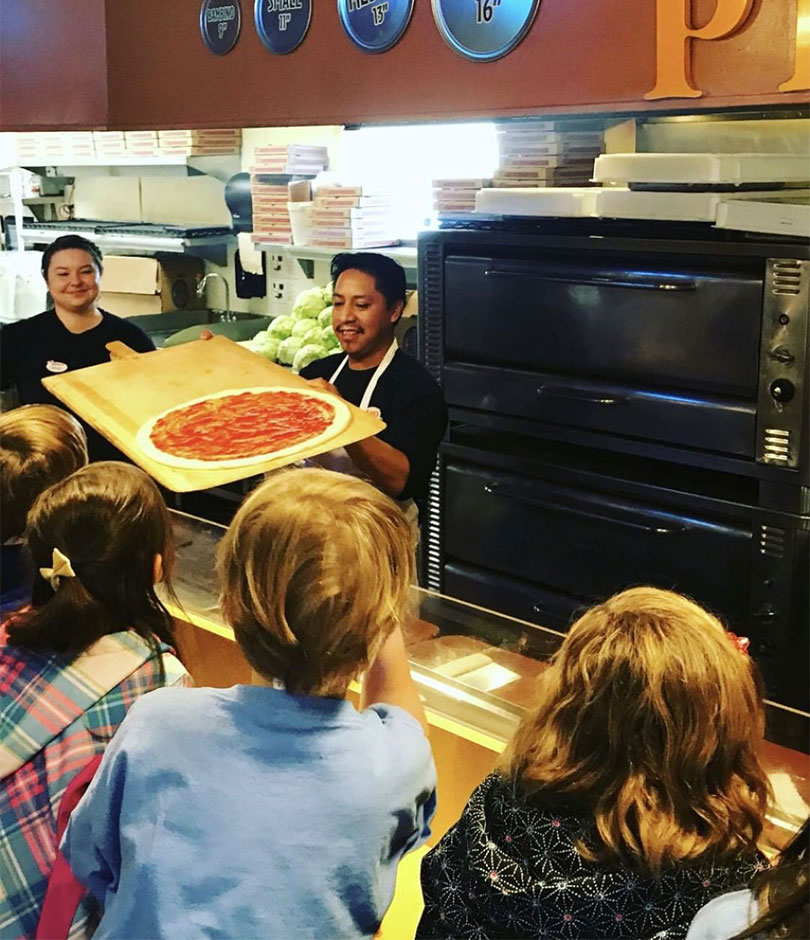 A man pulls out a fresh pizza to show kids at a waiter gives customers pizza at Mary's Pizza Shack